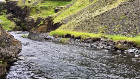 Stetig-Fließender-Fluss,-Der-Sich-Entlang-Grüner-Berghänge-Schlängelt,-Breite-Statische-Aufnahme