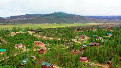 Aerial-Drone-View-of-a-Small-Mountain-Town-with-Houses-Surrounded-by-Lush-Summer-Forests-in-the-Rocky-Mountains-at-a-High-Elevation