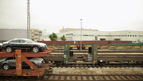 Cars-loaded-on-a-train-carriage-for-transport,-industrial-setting,-overcast-day
