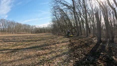 POV---Approaching-a-man-on-utility-tractor-towing-a-rototiller-to-loosen-soil-in-a-deer-food-plot-between-timber-and-field-in-early-spring