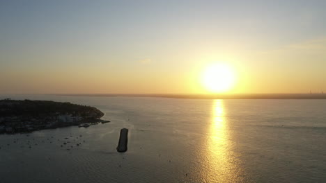 Aerial-shot-of-the-sun-setting-over-the-ocean-on-the-coast-of-the-Isle-of-Wight,-calm-sunny-day