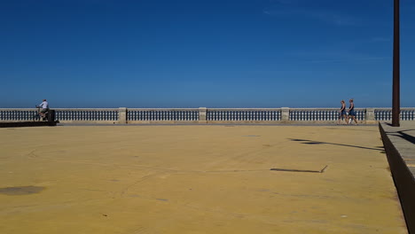 Cadiz,-Spain,-People-Walking-on-Promenade-Square-by-Atlantic-Ocean-on-Hot-Summer-Day