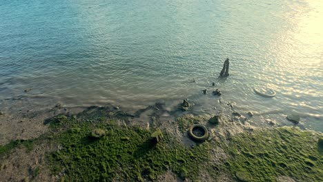 Car-tires-rest-silently-by-the-water,-illuminated-by-the-soft-glow-of-the-setting-sun,-painting-a-poignant-picture-of-wear-and-tear,-echoing-the-passage-of-time-and-the-relentless-forces-of-nature