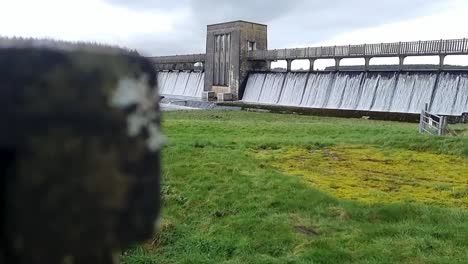 Cefni-dam-slow-motion-rising-to-reveal-establishing-overflow-barrier-pouring-from-Llangefni-countryside-reservoir