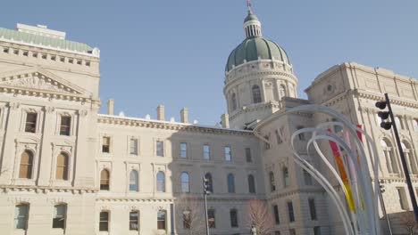 Outside-of-Indiana-state-capitol-building-in-Indianapolis,-Indiana-with-art-work-and-people-walking-with-video-panning-right-to-left-and-down