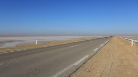 Carretera-Vacía-Del-Desierto-Que-Se-Extiende-Hasta-El-Horizonte-Bajo-Un-Cielo-Azul-Claro,-Túnez