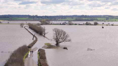 Menschen-Gehen-Auf-Einer-Ländlichen-Landstraße-In-Der-Nähe-Eines-Vom-Hochwasser-Völlig-Abgeschnittenen-Hauses