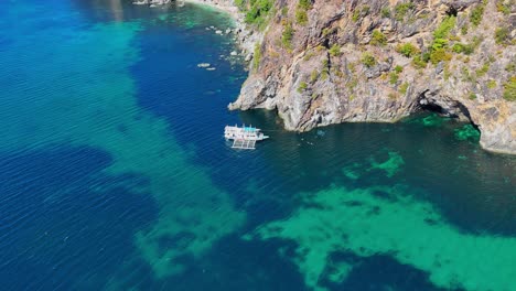 Drone-footage-of-steep-cliffs,-turquoise-water-and-a-boat-near-Palawan-in-the-Philippines