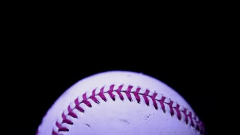 Spotlight-moves-across-baseball,-luminating-up-red-lace-stitching