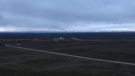 Drone-flying-across-barren-desert-landscape-at-overcast-cloudy-dusk-cars-driving-very-fast-on-highway