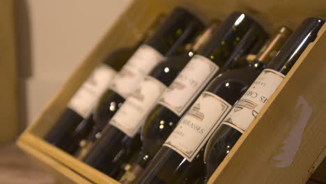 Close-up-of-six-dark-red-wine-bottles-in-wooden-case,-rack-focus