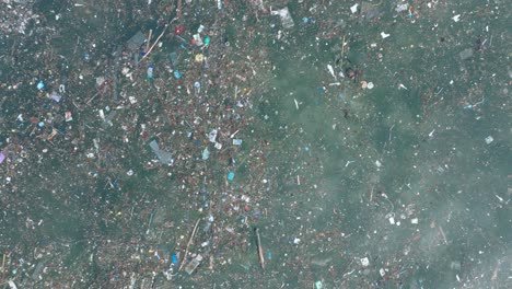 Low-altitude-top-down-panning-drone-shot-of-polluted-water-filled-with-trash-floating-over-dead-coral-reef-in-the-turqouise-tropical-water-of-Bali-Indonesia