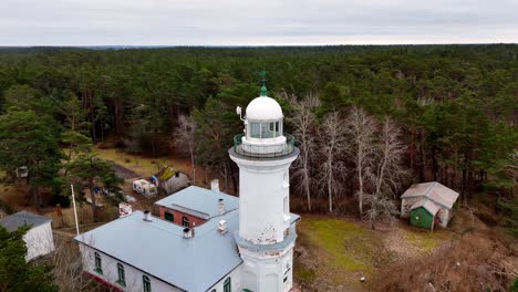 Uzava-lighthouse-in-Baltic-Sea-coast-standing-tall-amidst-a-dense-green-forest,-with-a-cloudy-sky-above