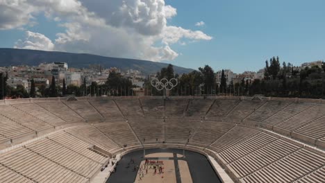 Vista-Aérea-Cinematográfica-Del-Monumental-Estadio-Panatenaico-De-Atenas-Con-Los-Anillos-Olímpicos-En-El-Centro,-Imágenes-De-Drones