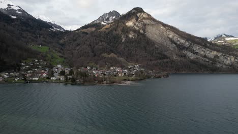 Aerial-static-of-windswept-lake-in-Switzerland-with-coastal-community-on-shoreline-below-snowy-mountains