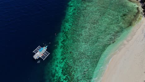 Top-down-drone-footage-of-a-boat-with-swimmers-in-turquoise-water-in-the-Philippines