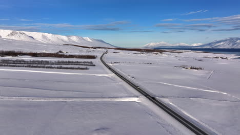 Vista-Aérea-De-Automóviles-Circulando-Por-Una-Carretera-De-Fiordo-En-Akureyri-Islandia-En-Un-Soleado-Día-De-Invierno