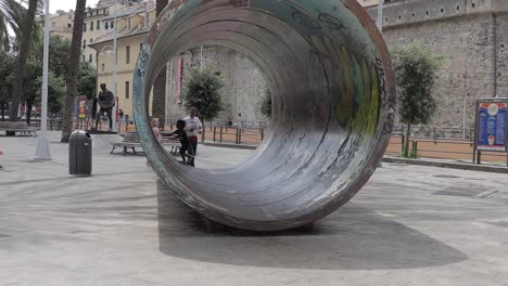 Handheld-clip-of-mum-and-2-young-children-playing-in-large-circular-art-installation-in-Genoa,-Italy