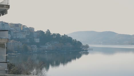 A-pan-right-tripod-movement-of-a-small-town-landscape,-transition-over-the-lake,-clear-water,-sunny-weather,-green-forest-trees-on-the-mountain,-European-buildings,-4K-video