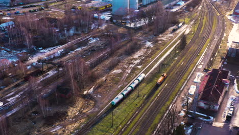 Railway-station-with-standing-cars-and-engine,-grain-silos-in-the-background,-aerial-flyover,-Valmiera,-Latvia