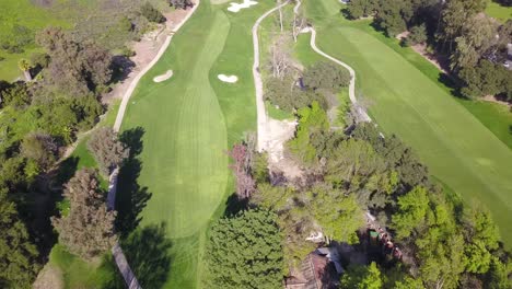 4K-Luftaufnahme-Eines-Wunderschönen-Golfplatzes-Unter-Prestigeträchtigen-Bedingungen-Mit-Bergen-Und-Sanften-Hügeln-Im-Hintergrund-An-Einem-Warmen,-Sonnigen-Tag