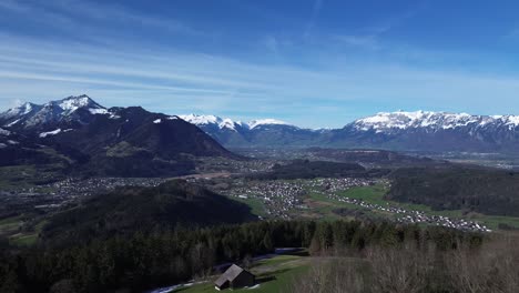 Drone-shot-of-huts-in-the-mountains-with-amazing-view-over-winter-mountain-landscape-with-snowcapped-mountains-on-a-sunny-day