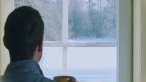 Lonely-man-drinking-coffee-on-a-cold-winter-snowy-day,-looking-out-window