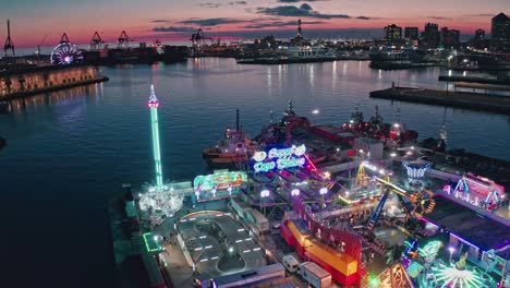 Neon-illuminated-rides-at-Genoa-Winter-Park-on-Ponte-Parodi,-twilight-aerial