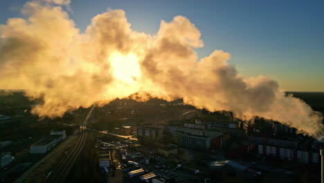 Steaming-chimney-vapour-emissions-floating-across-factory-refinery-during-sunset-aerial-drone-footage