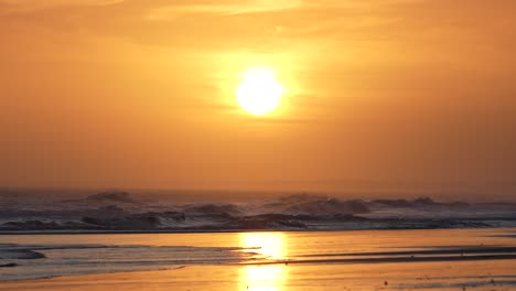 Golden-sun-setting-over-ocean-horizon-with-reflection-on-water,-slow-motion-capture-of-gentle-waves