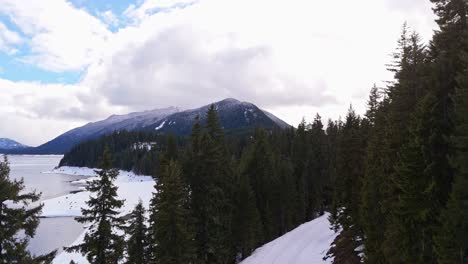 Revealing-view-of-Lake-Kachess-with-snow-bank-over-evergreen-trees-and-snowcapped-mountains-in-Washington-State