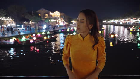 Woman-in-yellow-Ao-Dai-overlooking-lantern-lit-river-in-Hoi-An-at-night,-reflecting-cultural-essence