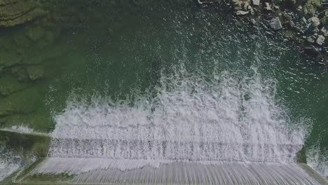 Una-Vista-Aérea-Hacia-Abajo-De-Una-Cascada-Artificial-Para-Un-Molino,-En-Un-Día-Soleado