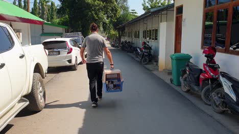 Un-Hombre-Caminando-Por-La-Calle-Llevando-Un-Gato-En-Una-Caja-De-Transporte-Para-Mascotas-Después-De-Un-Chequeo-Médico-Veterinario-E-Inspección-En-Preparación-Para-Volar-Y-Viajar-A-Un-Destino-En-El-Extranjero