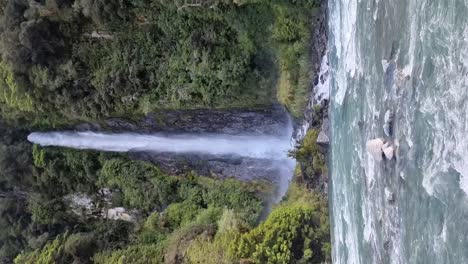 Vertikale-Ansicht-Der-Berühmten-Thunder-Creek-Falls,-Umgeben-Von-Regenwald-Und-Dem-Gletscherfluss,-Der-Davor-In-Haast-An-Der-Westküste-Neuseelands-Fließt