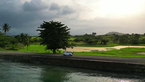 Following-a-car-on-the-coast-at-a-sunny-day,-surrounded-by-a-magnificent-green-landscape-at-São-Tomé,Africa