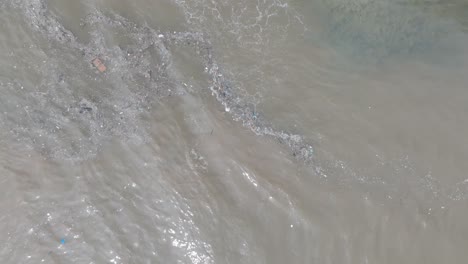 Drone-Aéreo-De-Arriba-Hacia-Abajo-Disparado-Sobre-Aguas-Residuales-Contaminadas-Y-Basura-Flotante-Con-Escombros-Sobre-Arrecifes-De-Coral-Muertos-Mezclándose-Con-Agua-Turquesa-Y-Costa-Tropical-En-Bali-Indonesia