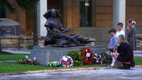 The-young-generation-of-Australians-paying-tribute-to-those-who-served,-standing-in-front-of-the-World-War-II-Nurses-Memorial-Statue-adorned-with-flowers-and-wreaths-at-Anzac-square