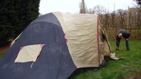 Man-using-tent-pegs-and-guy-ropes-with-an-old-tent