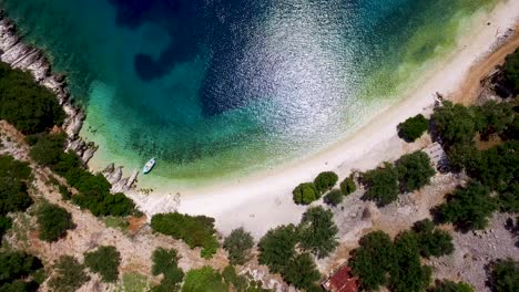 Orbiting-drone-shot-of-the-stunning-crystal-clear-waters-and-white-pebbles-of-Foki-Beach,-located-just-a-few-kilometers-from-the-world-famous-Fiskardo-village,-in-Greece