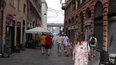 Groups-of-people-walking-along-narrow-paved-street-with-traditional-buildings-and-shops-at-the-sides