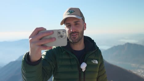 Male-Vlogger-Holding-Smartphone-Filming-Himself-On-Mountain-Top-In-Italy
