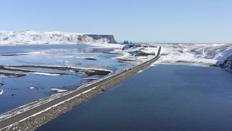 4k-Drone,-aerial-cinematic,-unique,scenically-beautiful-landscape-of-Iceland-with-long-stretch-of-the-road-surrounded-by-waters-melted-from-glaciers-and-the-rocky-mountain-cliff-at-the-distance