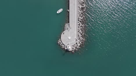 Top-view-of-beautiful-lighthouse-on-rocky-marina-with-a-small-boat