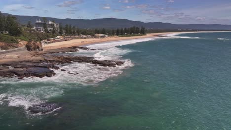 Aerial-reveal-over-the-ocean-of-North-Wollongong-Beach-and-the-surf-covered-rocks-below