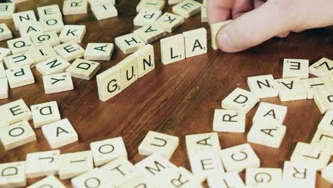 Bright-Scrabble-tile-letters-on-edge-form-words-GUN-and-LAWS,-close-up