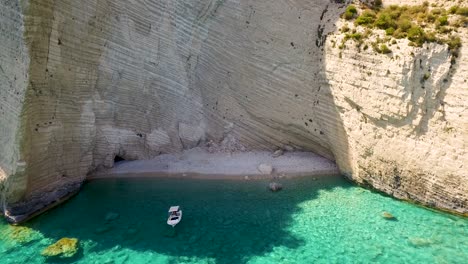 Drone-panning-from-the-left-to-the-right-side-of-the-frame,-showing-the-massive-rock-face-engulfing-the-secluded-beach-of-Oasi,-in-the-village-of-Chania,-located-in-the-island-of-Crete,-Greece