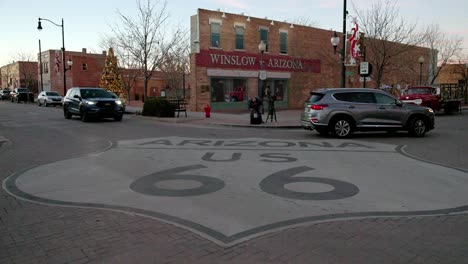Route-66-sign-at-an-intersection-in-Winslow,-Arizona-with-vehicles-and-pedestrians-with-stable-video