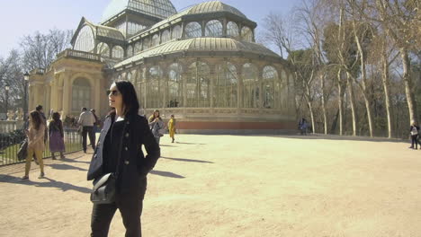 Mujer-Explorando-El-Palacio-De-Cristal-En-Un-Día-Soleado-En-El-Parque-Del-Retiro,-Madrid,-Rodeada-De-Visitantes-Tranquilos