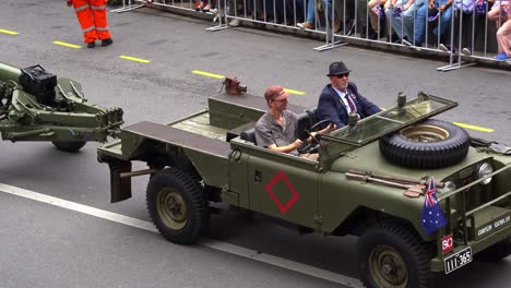 A-military-vehicle-with-an-artillery-trailer-drives-down-the-street,-participating-in-the-annual-Anzac-Day-parade
